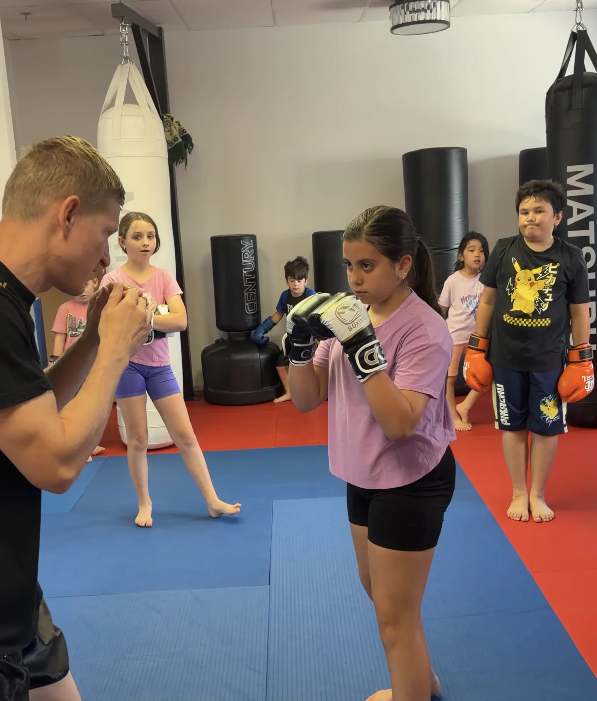 A coach holding focus mitts for a child in boxing gloves at a kids Muay Thai class